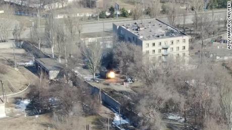 This screenshot of the drone footage shows a military vehicle firing gunshots near a building.
