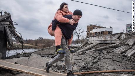 A man holds a woman as they cross an impromptu road as they flee Irben, Ukraine on Sunday.