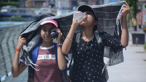 Girls cover their heads as they walk and drink water in the scorching afternoon heat of Mumbai.