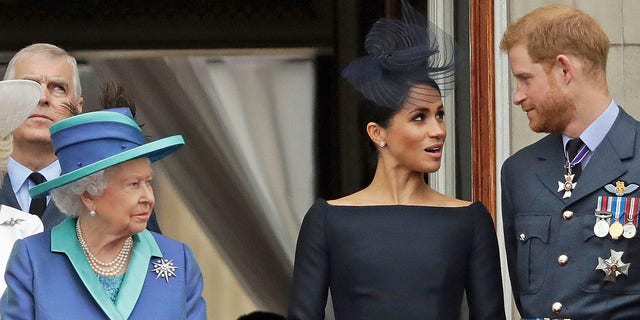 Queen Elizabeth, Meghan Markle and Prince Harry stand on a balcony to watch an RAF fly over Buckingham Palace in 2018.