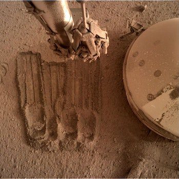 In another recent photo, InSight uses its robotic arms to remove some of the perimeter of the regolith...